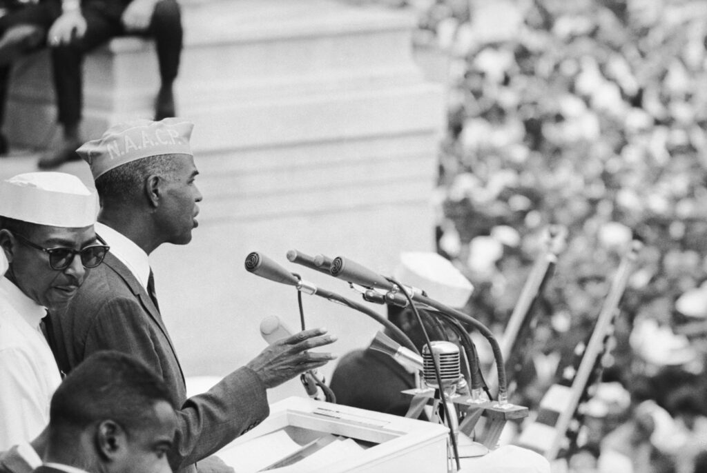 A man in an NAACP hat standing at a microphone speaking to a crowd
